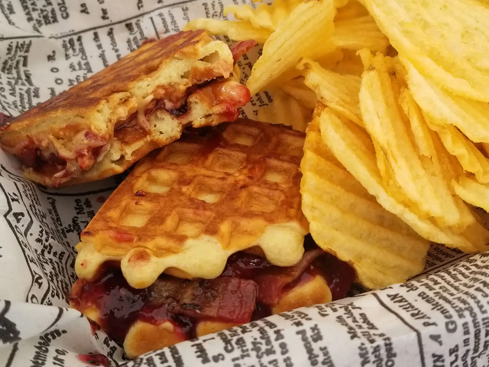 A waffle sandwich with cheese and bacon, and a side of kettle chips