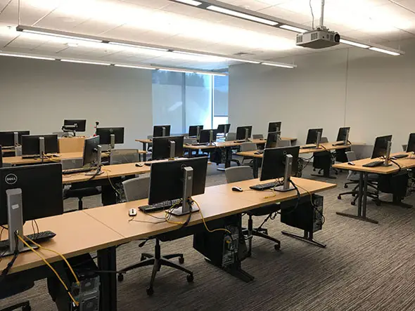 Rows of tables with silver chairs and computers in a windowed computer lab on the Oregon City campus