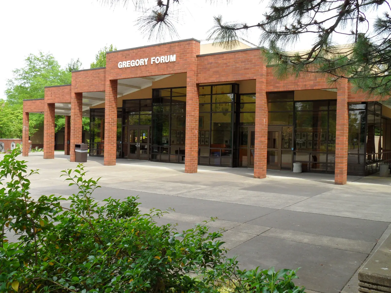 The entrance to Gregory Forum, featuring brick arches, full walls of glass and leafy surroundings at the Oregon City campus