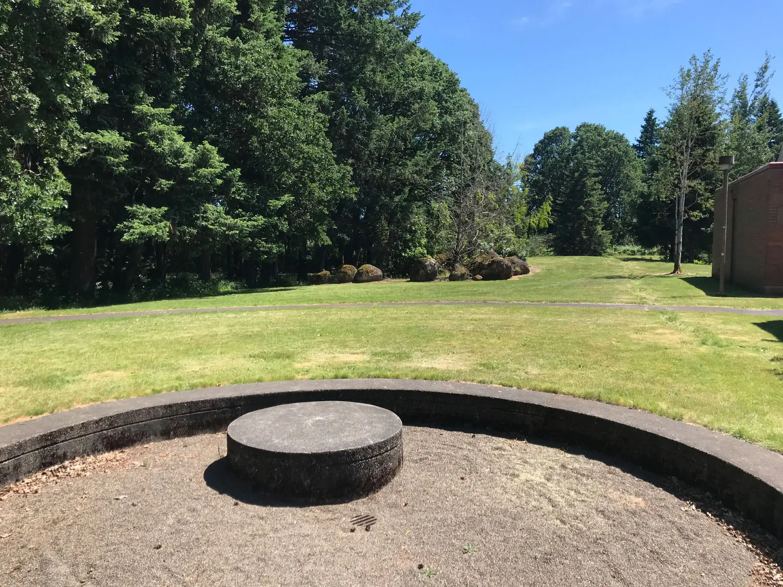 A circular, stone structure pit with sand in an open field on the Oregon City campus