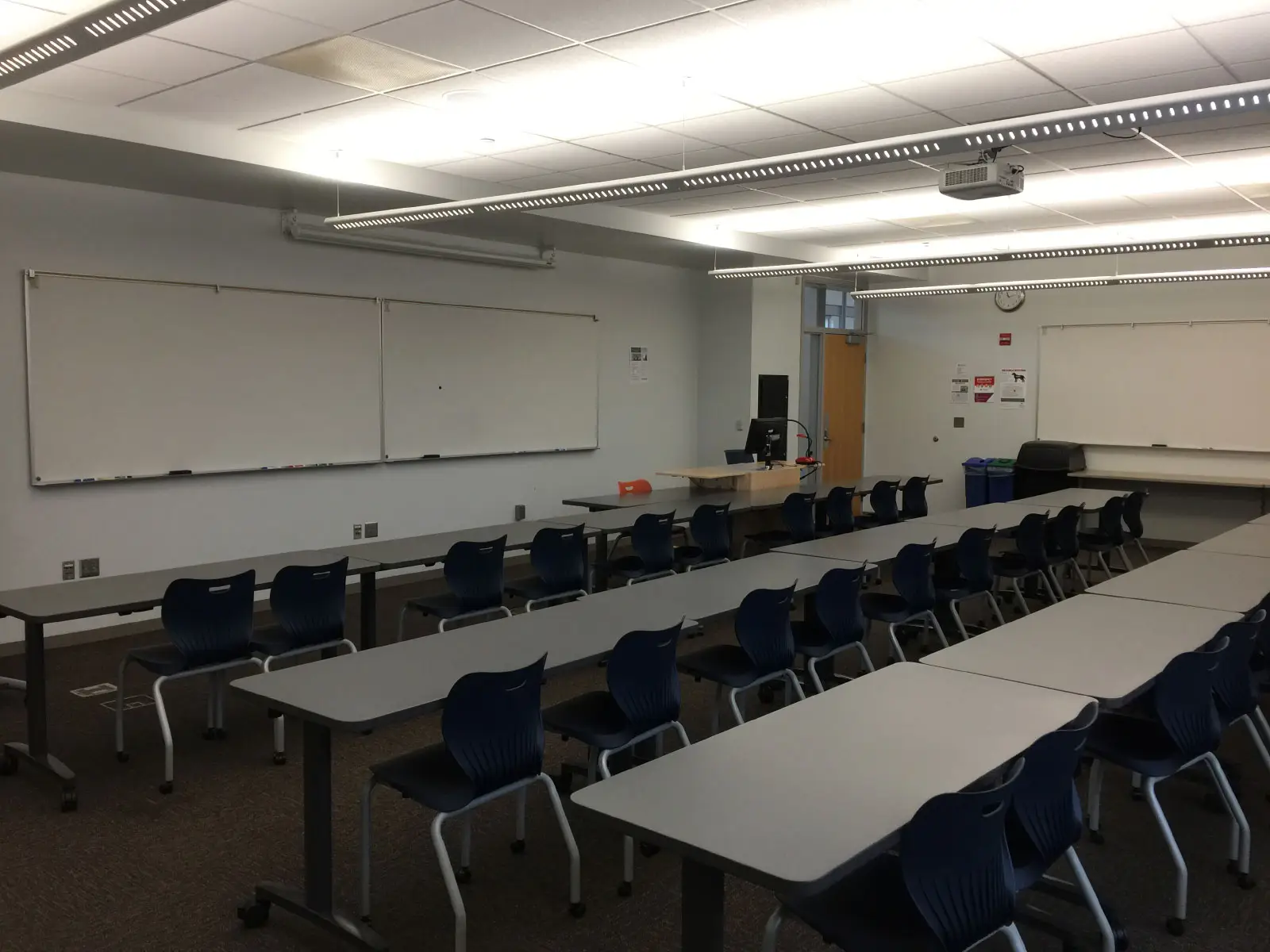 Rows of blue chairs and tables in front of a podium and white board in classroom W210 on the WIlsonville campus