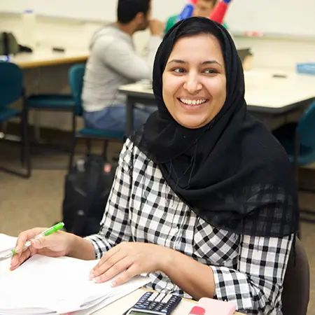 CCC student smiles while looking up from a notebook and calculator on the table