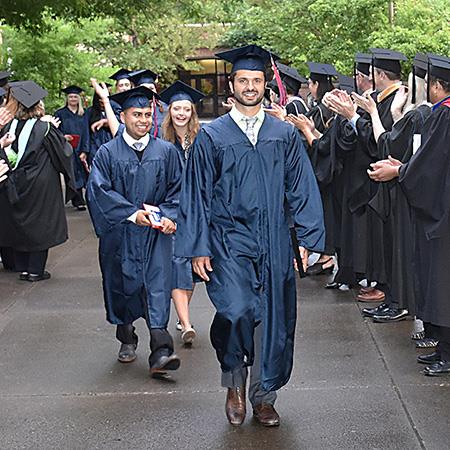 graduate in cap and gown walks through line of applauding faculty