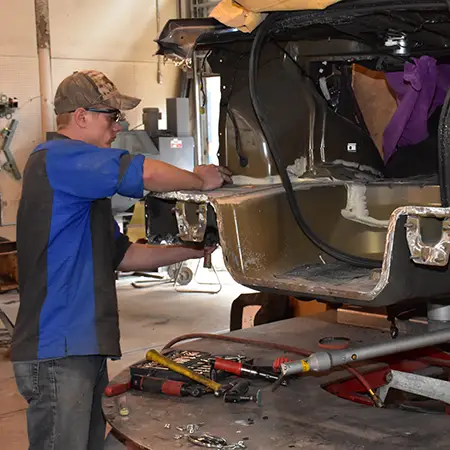 Auto repair technician works on the metal frame of a car.