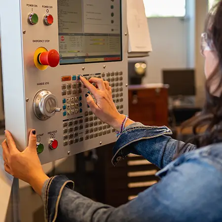 A student pushes buttons on a panel to operate computer-aided manufacturing equipment.