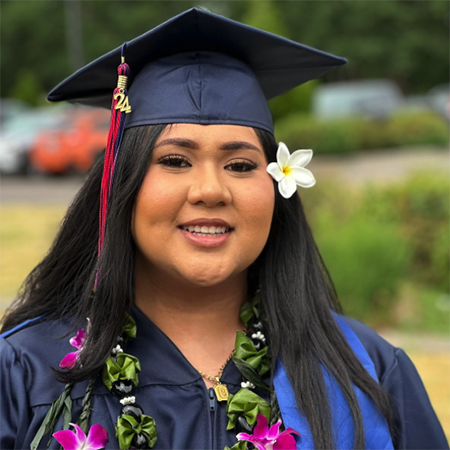 Clackamas Community College graduate smiles wearing cap and gown and flowers