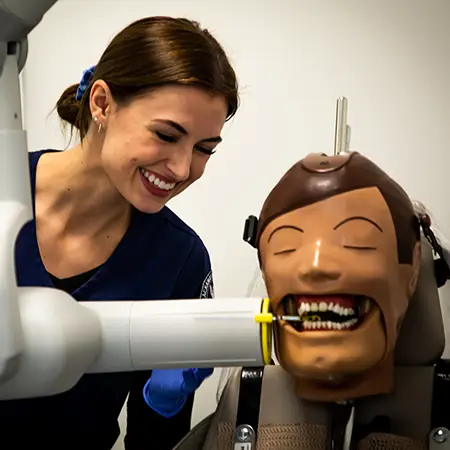 Smiling dental assistant student works with a training prop.