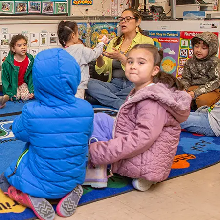 El maestro interactúa con el aula de niños pequeños sentados en círculo.