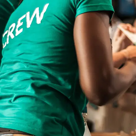 An employee working while wearing a teal shirt that says "Crew" on the back of it.