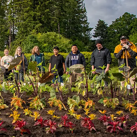 A line of horticulture students posing behind rows of young inground plants at the Oregon City campus.