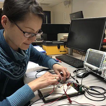 Microelectronics student working on a small circuit board full of connection points, lights and wires.