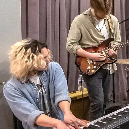 Student musicians practicing in a CCC studio - one student is playing a keyboard and the other is playing an electric guitar.