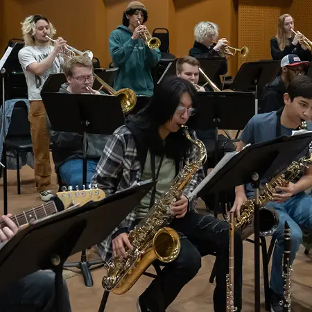 Group of music students playing together with trumpets in the back and saxophones in the front.