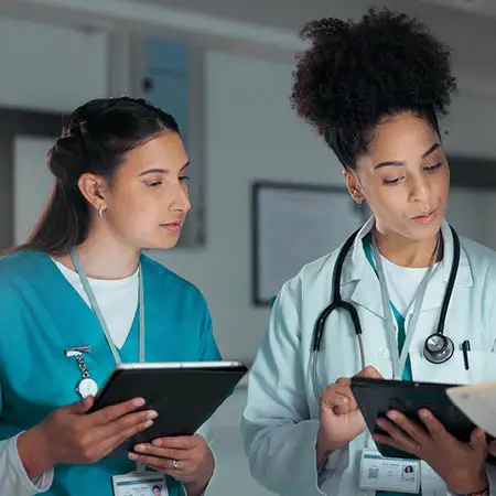 Health care provider in lab coat and stethoscope reviews documents with another provider wearing scrubs