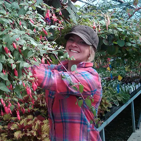 Student tending to a hanging plant with pink flowers in a greenhouse at the Oregon City campus.