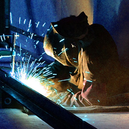 Sparks fly as a welder in safety equipment does welding work on a metal beam.