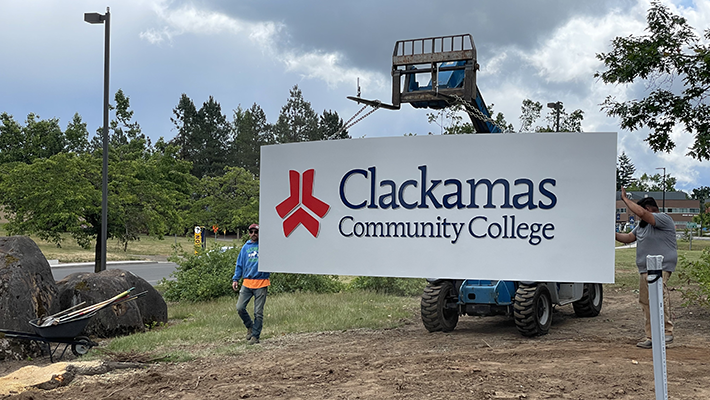 Workers use a forklift to install a large Clackamas Community College sign